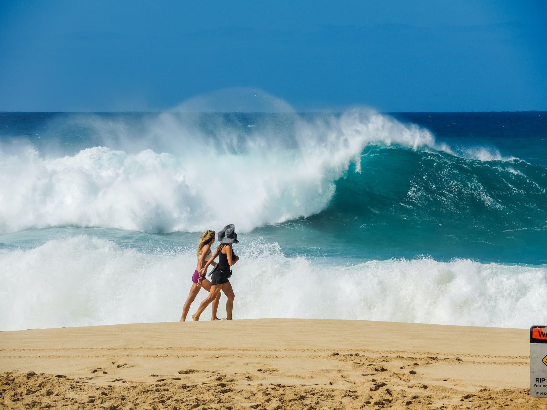 haleiwa hullámai az óceánparton sétáló nők mögött oahu szigetén